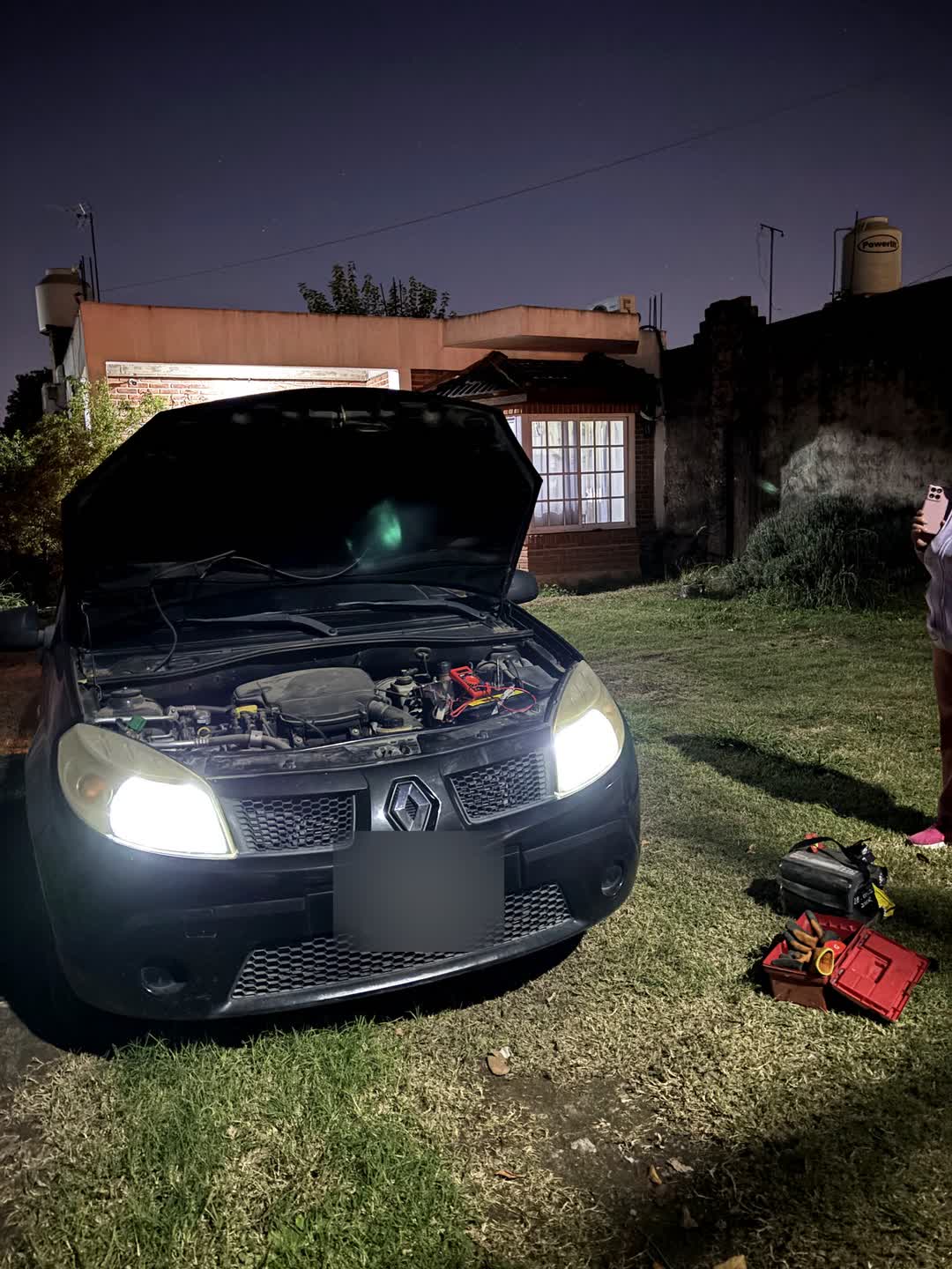 Auto de noche con el capó abierto y las luces encendidas, durante un auxilio de batería