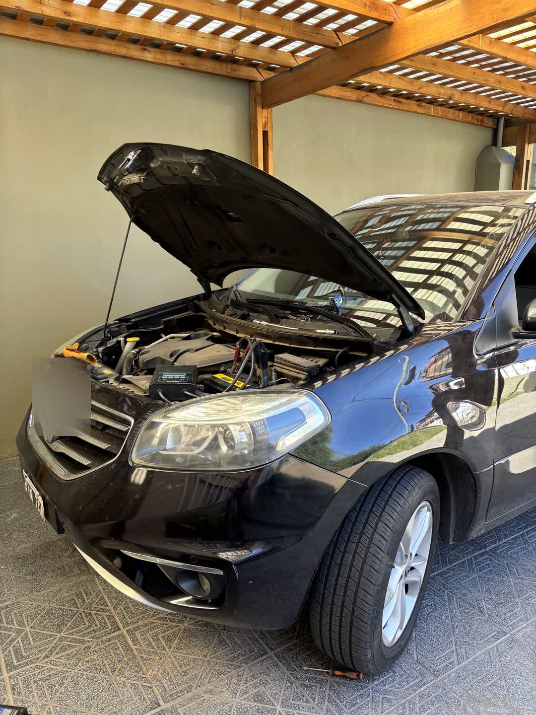 Auto con el capó abierto bajo un techo de cochera, durante un cambio de batería a domicilio
