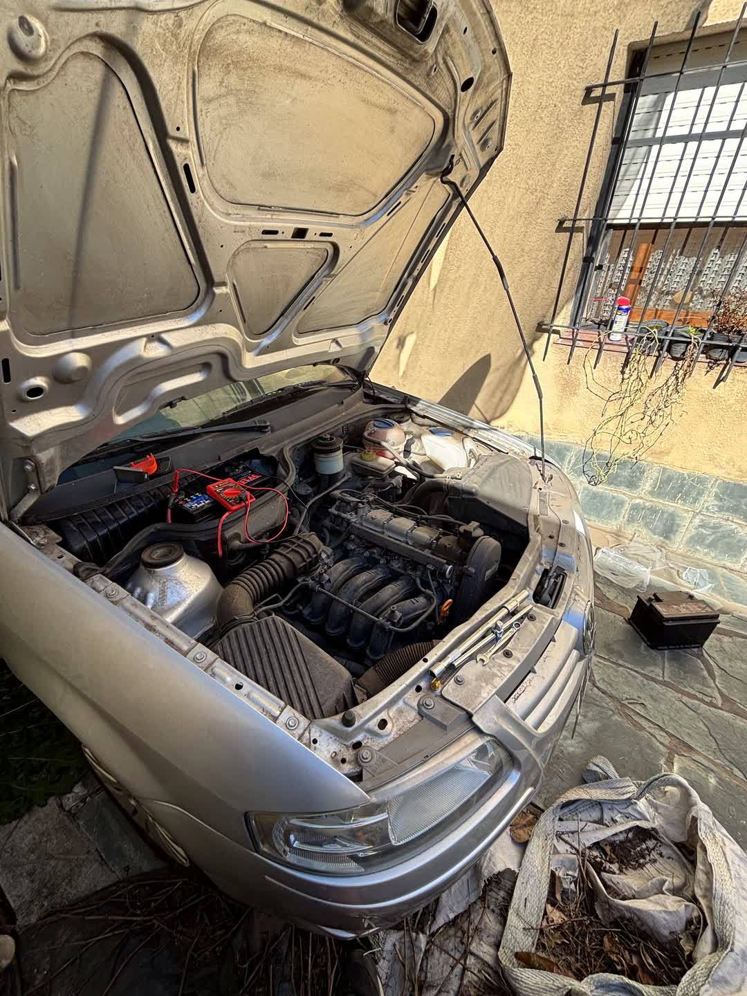 Auto plateado con el capó abierto en la vereda durante una colocación